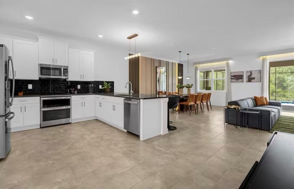 2992 Penelope Loop Kissimmee, FL 34746 - Photo 14 of 83 a kitchen with stainless steel appliances kitchen island granite countertop a refrigerator a stove a sink a dining table and chairs with wooden floor
