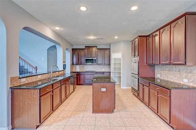 a large kitchen with stainless steel appliances kitchen island granite countertop a large counter top and a stove top oven