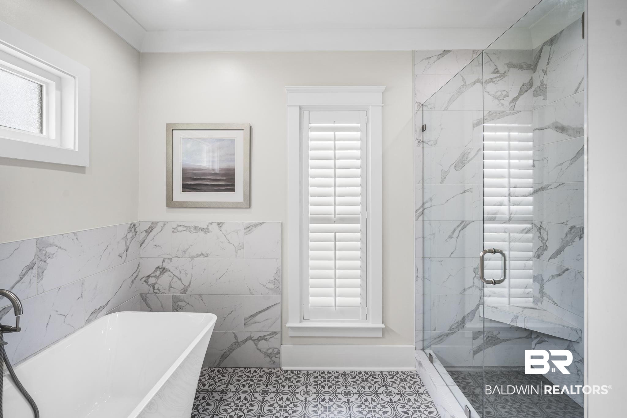 21702 Pillars Street Fairhope, AL 36532 - Photo 23 of 54 Freestanding soaking tub with floor-mounted faucet, marble-look tiled walls, glass-enclosed shower with built-in bench, patterned floor tiles, and a window with plantation shutters