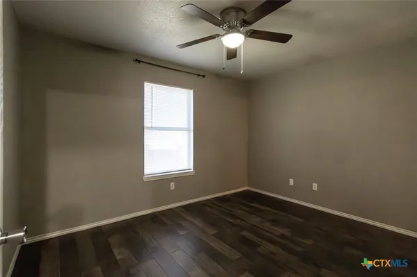 an empty room with wooden floor chandelier fan and windows