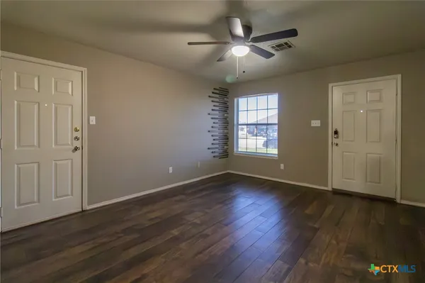 an empty room with wooden floor chandelier fan and windows