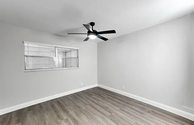 an empty room with wooden floor a ceiling fan and a window