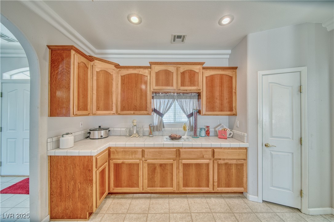 660 Indian Road Pahrump, NV 89048 - Photo 30 of 54 Kitchen with arched doorways, staggered alder wood cabs, crown moulding, pantry door, supplemental kitchen storage, tile workstation, and recessed lighting.