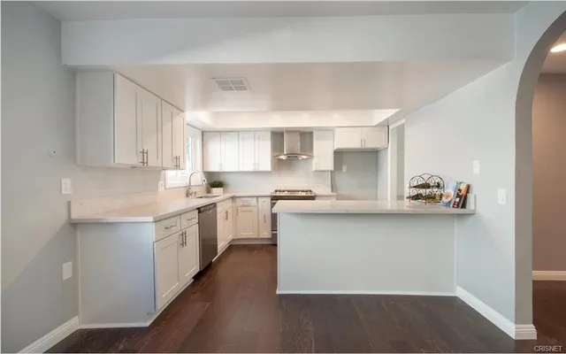 a kitchen with stainless steel appliances a sink dishwasher a refrigerator and white cabinets with wooden floor