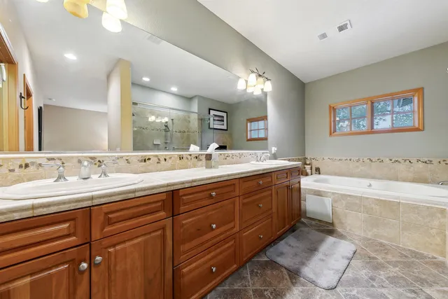 a spacious bathroom with a granite countertop double vanity sink a mirror and a bathtub