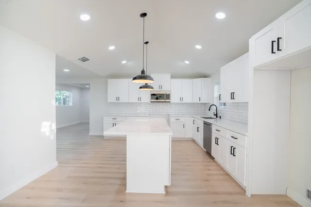 a large kitchen with stainless steel appliances kitchen island a stove a sink a refrigerator and white cabinets with wooden floor