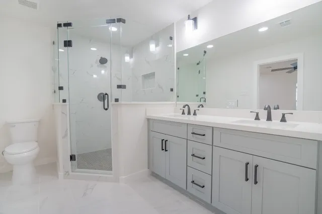 a spacious bathroom with double sink a toilet a shower and a mirror