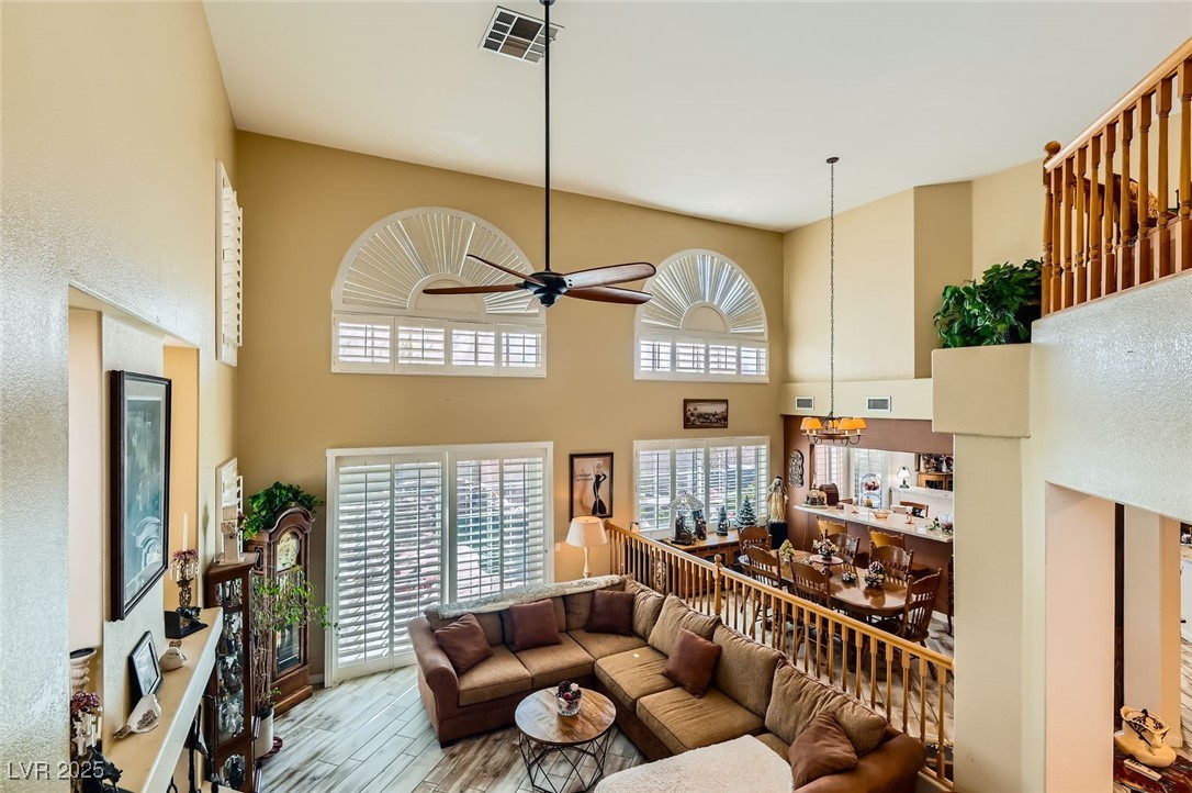 20 High Sierra Henderson, NV 89074 - Photo 13 of 53 Living area featuring ceiling fan with notable chandelier, a high ceiling, wood finished floors, and visible vents