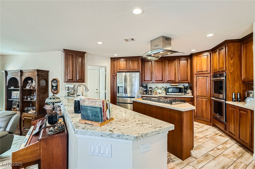 20 High Sierra Henderson, NV 89074 - Photo 18 of 53 Kitchen featuring visible vents, a center island, light stone counters, island exhaust hood, and stainless steel appliances