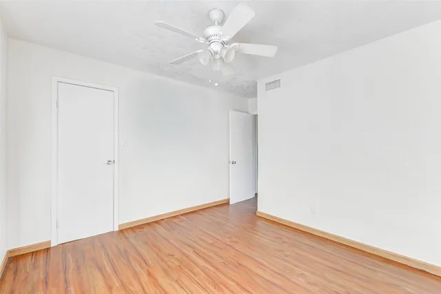 an empty room with wooden floor and a ceiling fan