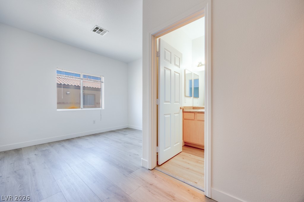 4915 East Russell Road, Unit 127 Las Vegas, NV 89120 - Photo 15 of 19 Laminate wood flooring sweeps across this inviting bedroom, with an adjacent bathroom vanity visible through the open doorway.