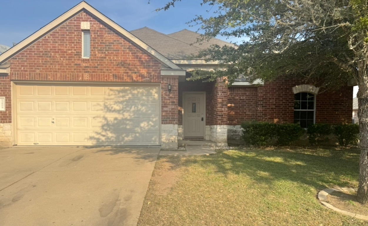 View of front of property with brick siding, driveway, a front yard, and a garage