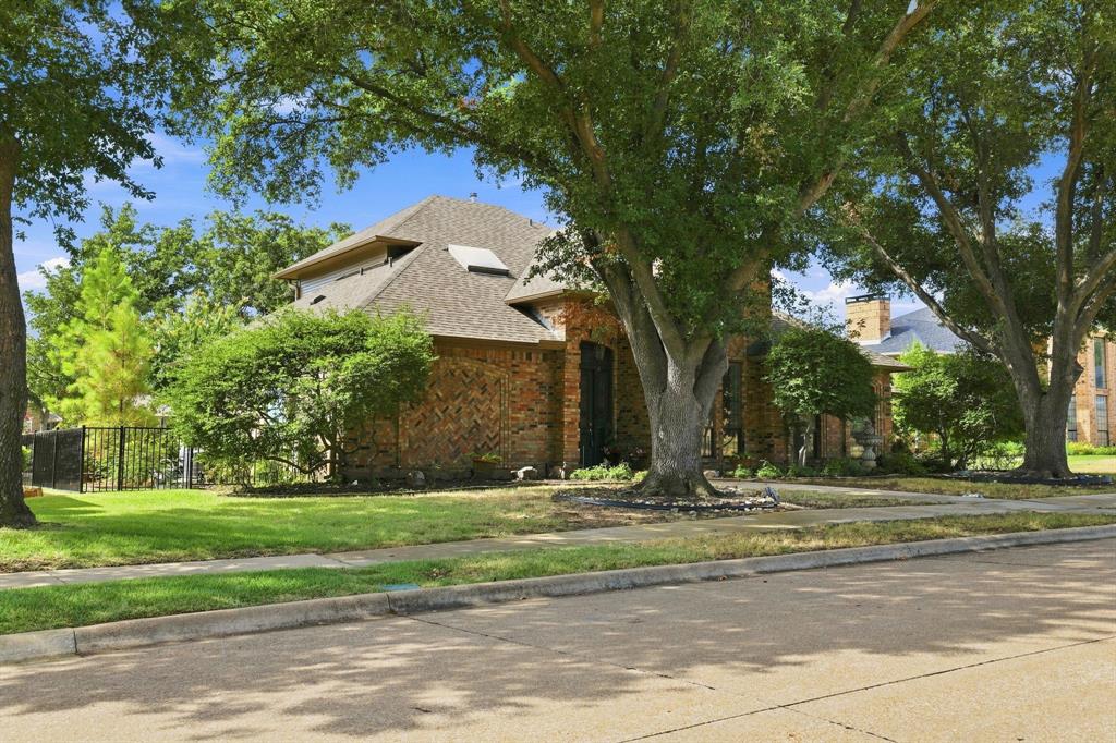 1762 Timber Ridge Circle Corinth, TX 76210 - Photo 2 of 29 Brick exterior with a gabled shingle roof, mature trees, and a decorative wrought iron fence