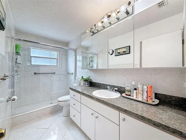 a bathroom with a granite countertop sink a toilet a mirror and shower