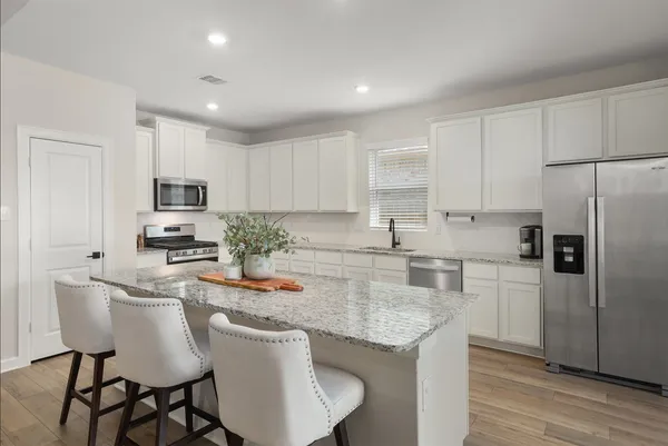 a kitchen with stainless steel appliances granite countertop a stove a sink a microwave a refrigerator and white cabinets