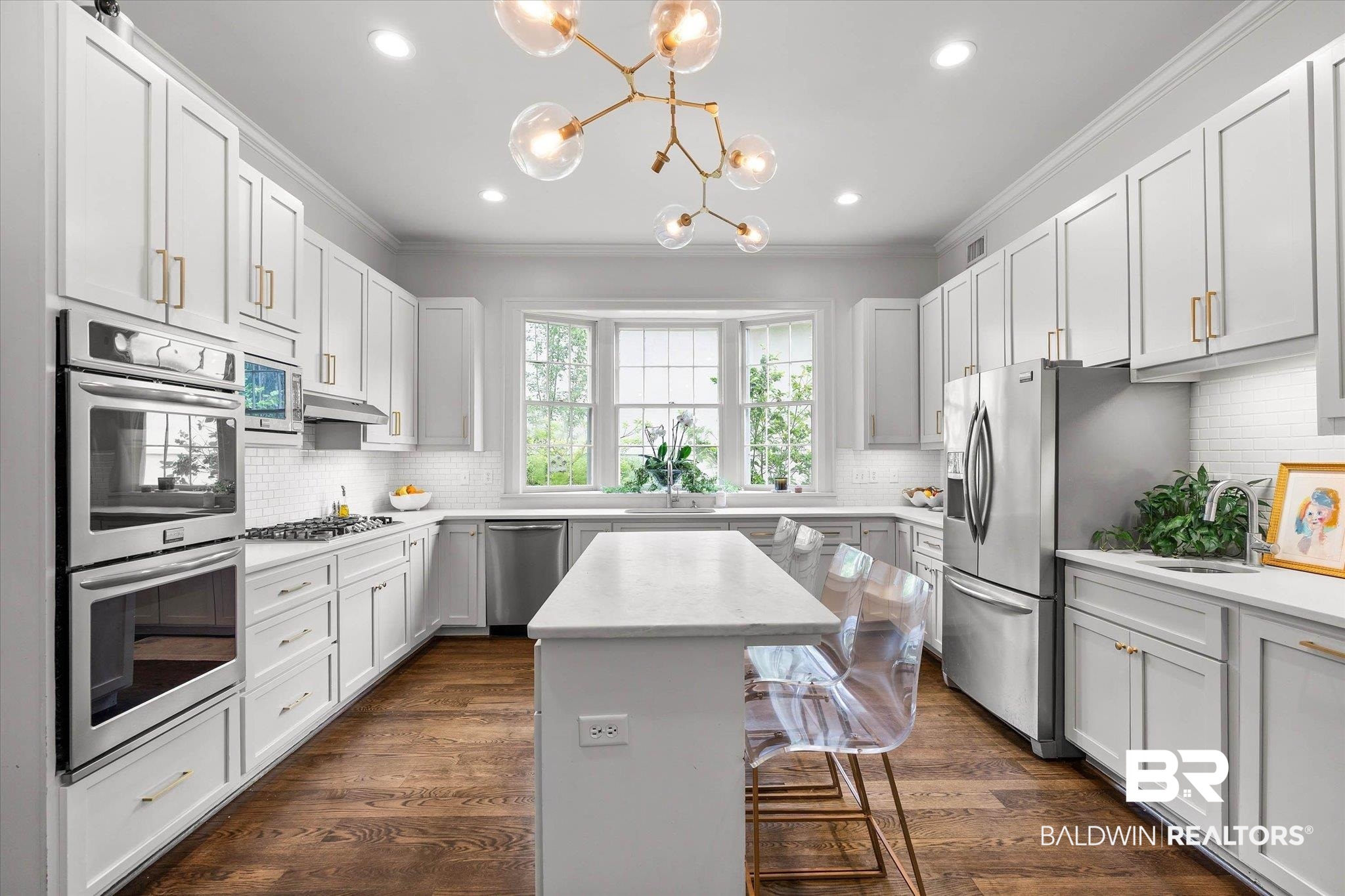 3908 Yester Place Mobile, AL 36608 - Photo 17 of 45 Modern kitchen featuring a central island with countertop seating, white shaker cabinetry, stainless steel appliances including double wall ovens, and wood-finish flooring