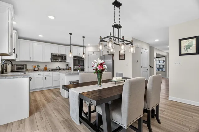 a kitchen with stainless steel appliances granite countertop a stove a refrigerator a kitchen island a dining table and chairs with wooden floor