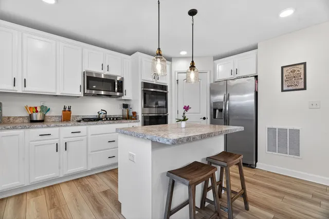 a kitchen with stainless steel appliances granite countertop a sink a microwave a refrigerator and white cabinets