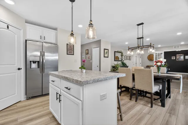 a kitchen with stainless steel appliances granite countertop a refrigerator a sink dishwasher a dining table and chairs with wooden floor