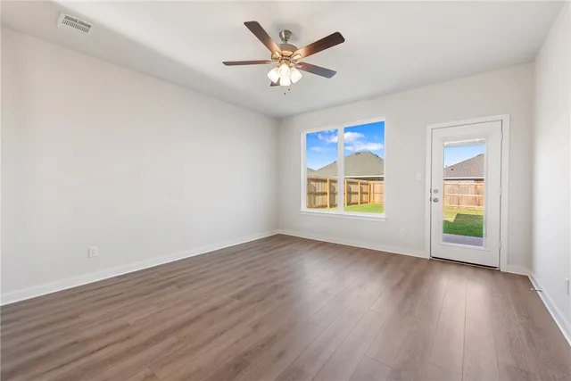 an empty room with wooden floor chandelier fan and windows