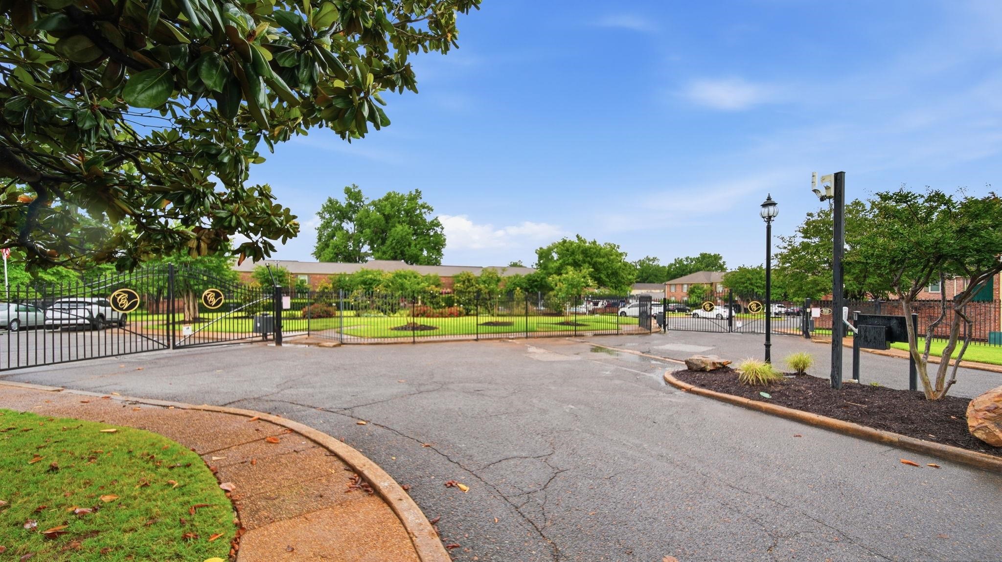 5866 Roxbury Drive, Unit 5866 Memphis, TN 38119 - Photo 16 of 20 Gated community entrance featuring wrought iron gates, a manicured lawn, mature trees, and a paved drive