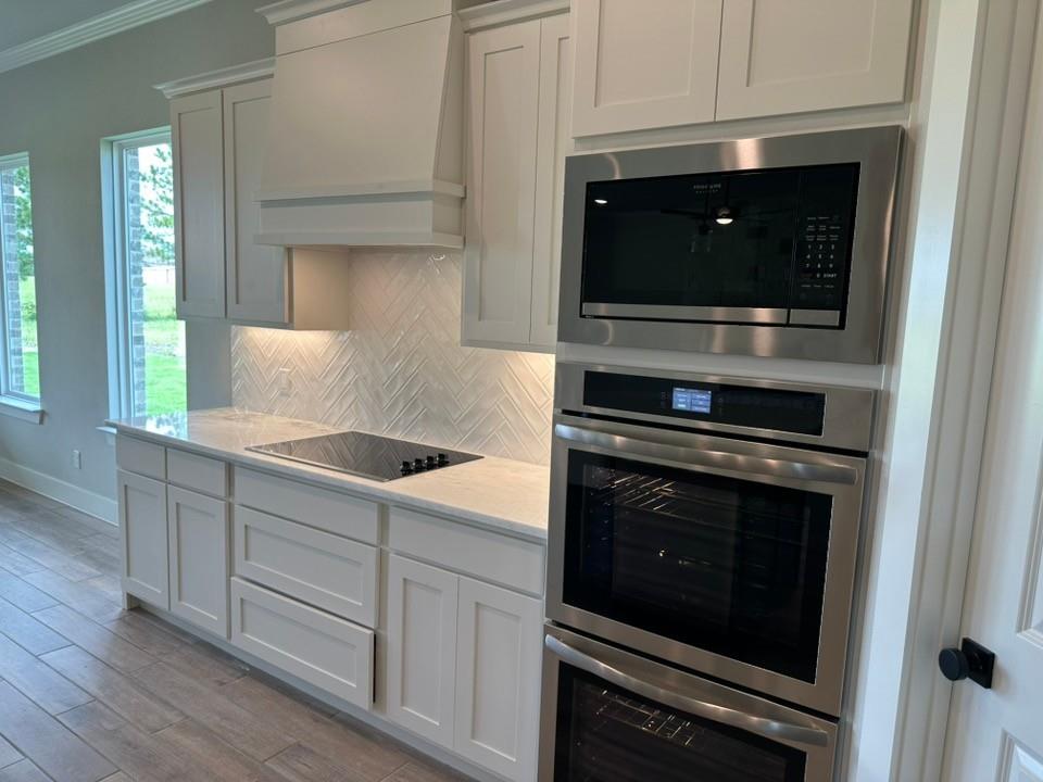 390 Cobb Road Leonard, TX 75452 - Photo 14 of 26 Modern kitchen with white shaker cabinetry, an integrated cooktop, stainless steel wall oven, stainless steel microwave, and wood-finish flooring