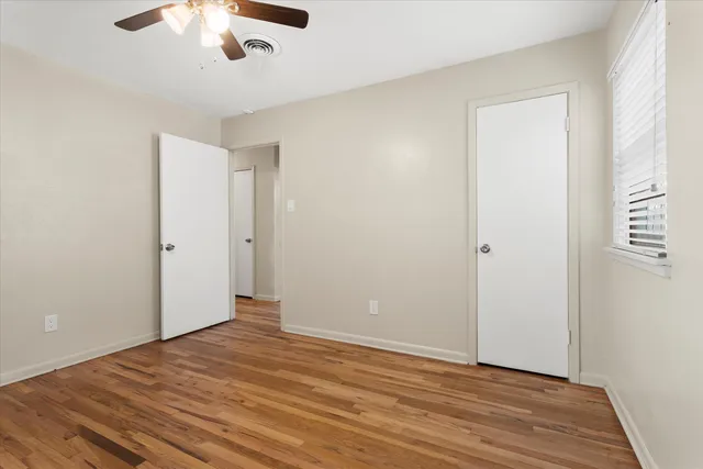 an empty room with wooden floor chandelier fan and windows