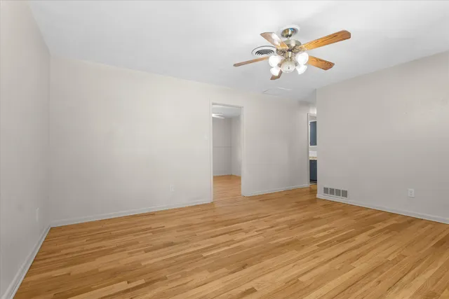 a view of an empty room with chandelier fan and wooden floor