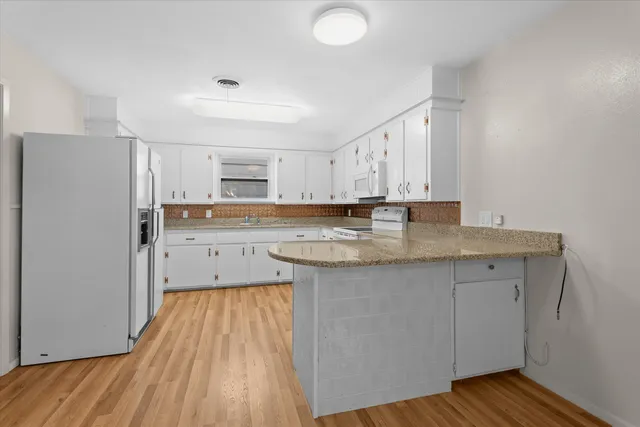 a kitchen with wooden floors white cabinets and refrigerator