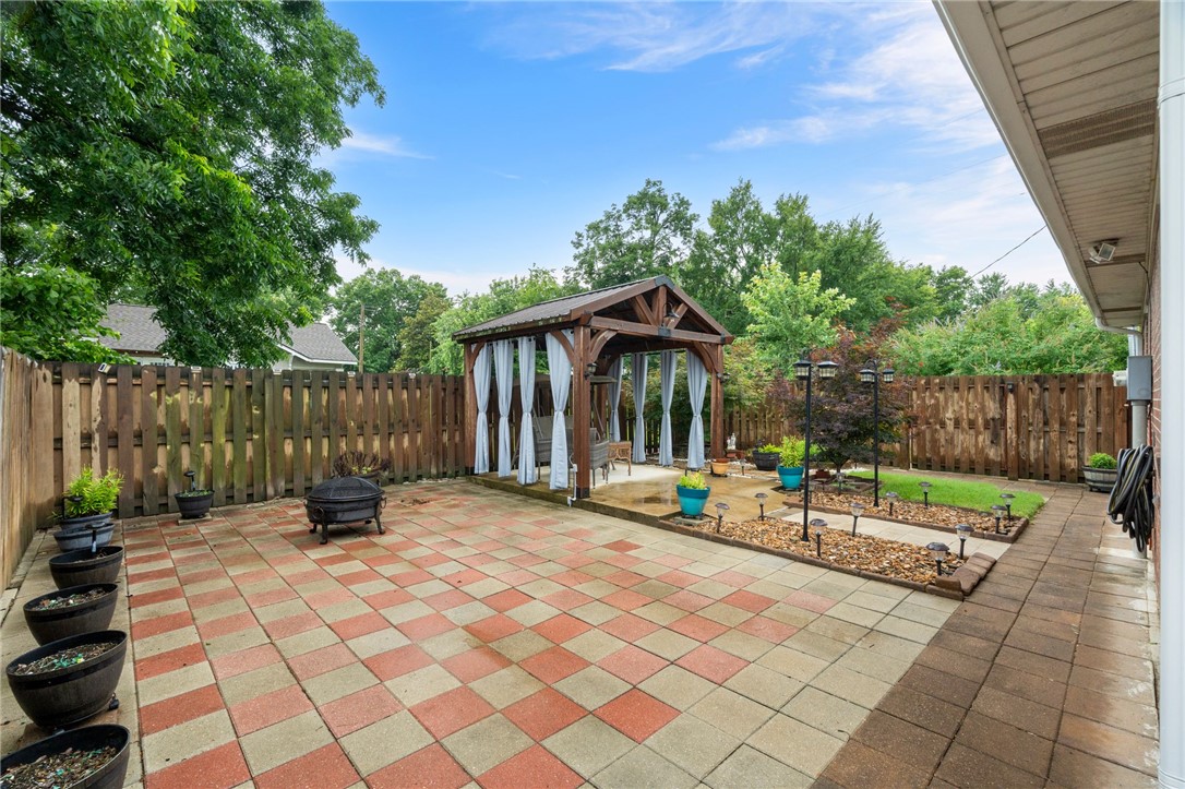 624 Locke Street Alma, AR 72921 - Photo 28 of 32 Spacious patio featuring a checkered paver design, a wooden gazebo with privacy curtains, and dedicated garden beds
