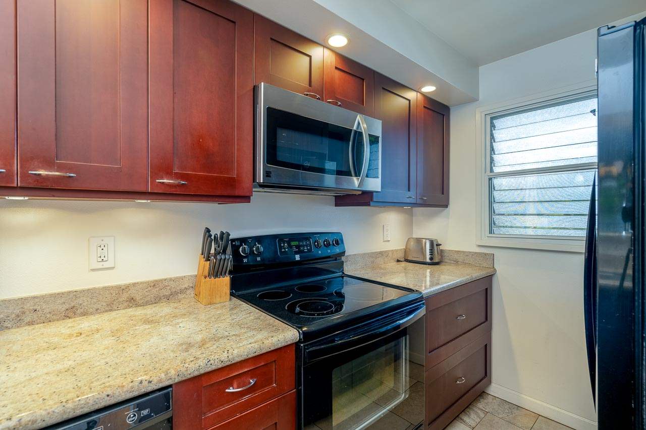 2430 South Kihei Road, Unit 206 Kihei, HI 96753 - Photo 11 of 26 a kitchen with granite countertop wooden cabinets and a stove top oven