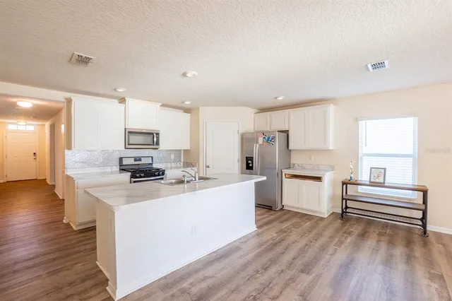 a kitchen with stainless steel appliances a stove top oven a sink a refrigerator white cabinets and wooden floor