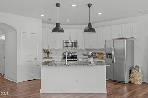 a kitchen with stainless steel appliances granite countertop a sink a stove a refrigerator and white cabinets with wooden floor