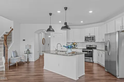 a open kitchen with stainless steel appliances granite countertop a stove top oven a dining table and chairs with wooden floor