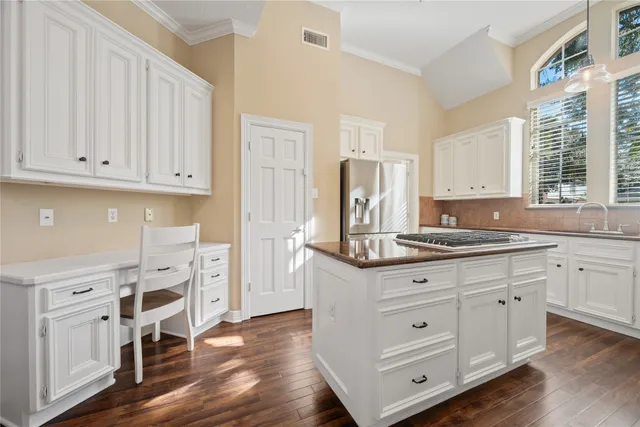 a kitchen with stainless steel appliances granite countertop a stove a refrigerator and white cabinets with wooden floors