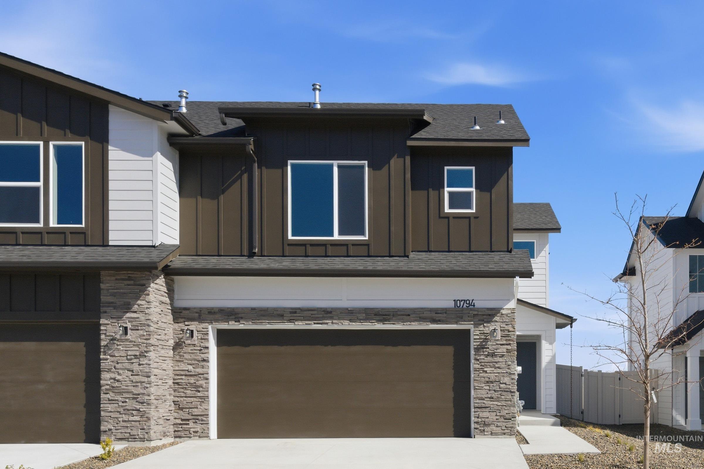 Modern townhome exterior featuring a brown vertical siding facade, white horizontal siding accents, stone veneer detailing, a dark shingle roof, and an integrated garage with a brown door