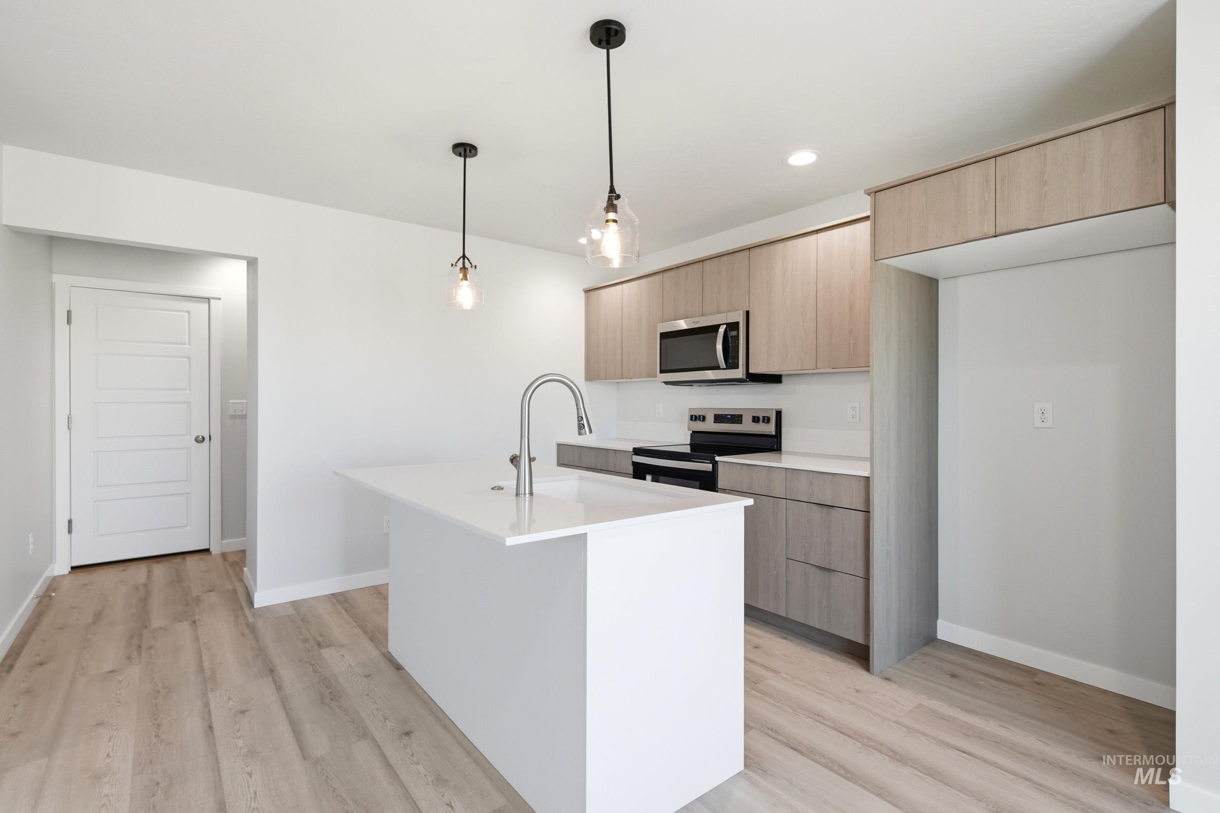 10794 Rutland Street Caldwell, ID 83605 - Photo 3 of 22 Modern kitchen featuring a central island with a gooseneck faucet, light wood-finish cabinetry, stainless steel appliances, and wood-finish flooring