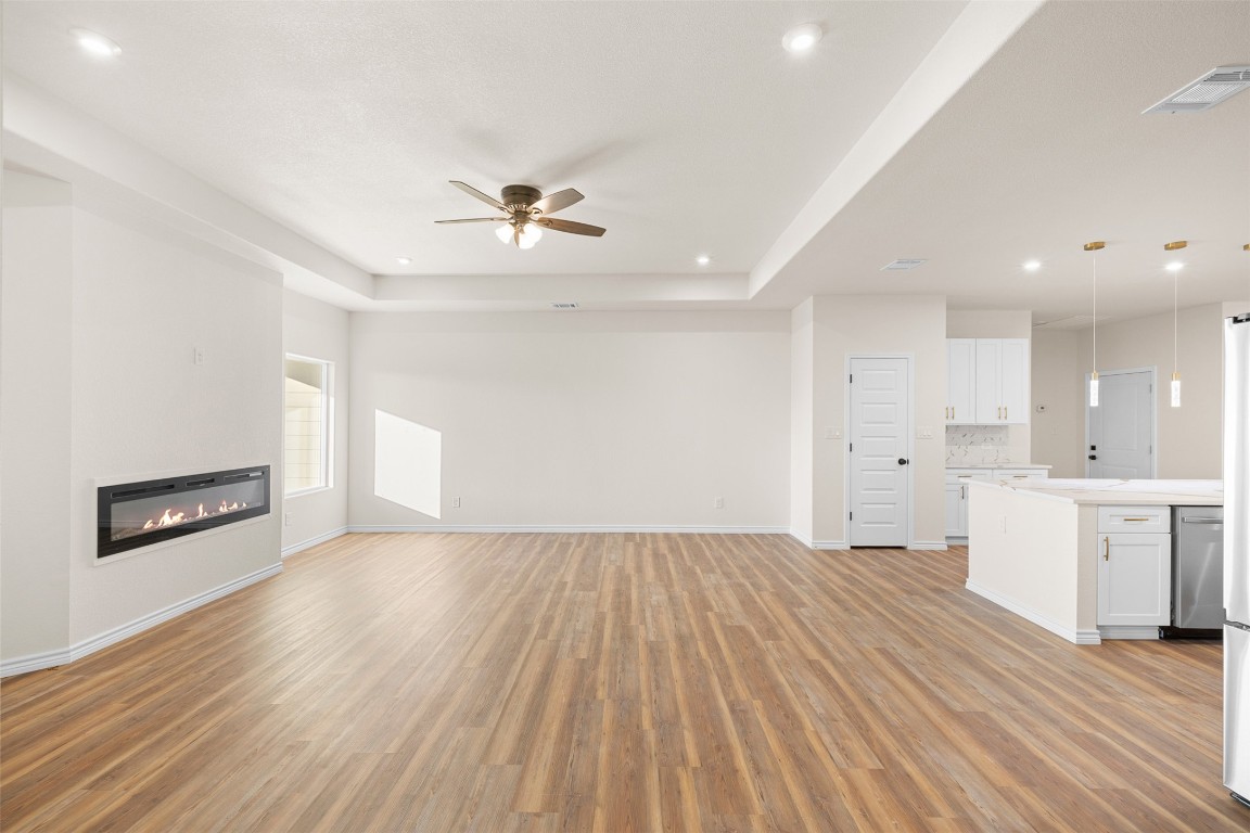 340 Cactus Street Giddings, TX 78942 - Photo 13 of 37 Unfurnished living room with a glass covered fireplace, light wood-style flooring, a raised ceiling, ceiling fan, and recessed lighting