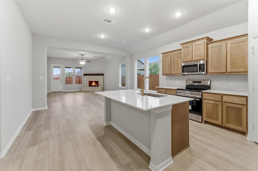 1237 Frio Drive Springtown, TX 76082 - Photo 7 of 25 Spacious open-concept kitchen and living area featuring wood-finish flooring, a contemporary kitchen island with a single-basin sink, light wood cabinetry, stainless steel appliances, and a stone fireplace