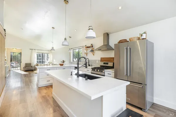 a kitchen with stainless steel appliances a refrigerator a sink dishwasher a oven with white cabinets and wooden floor
