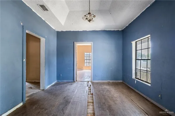 an empty room with a chandelier fan and wooden floor