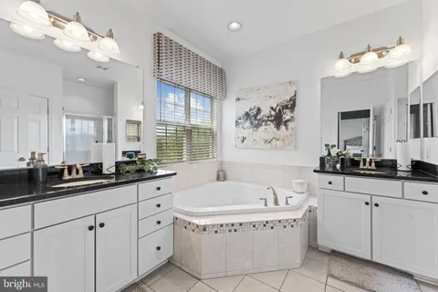 a spacious en suite bathroom with a granite countertop sink a large mirror and a bathtub