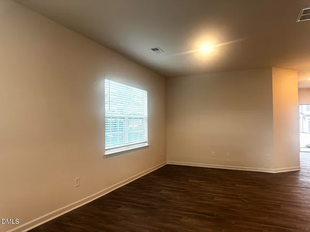 an empty room with wooden floor and a kitchen