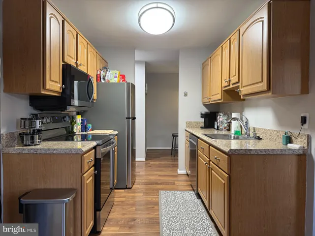 a kitchen with stainless steel appliances granite countertop a stove top oven a sink dishwasher and a refrigerator with wooden cabinets