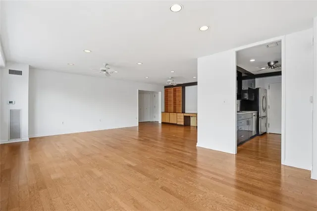 a view of an empty room with wooden floor and a kitchen