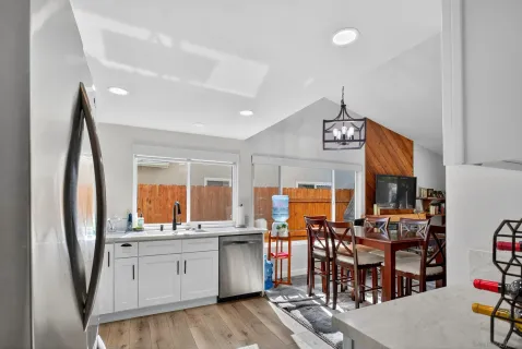 a kitchen with stainless steel appliances a refrigerator a sink dishwasher a dining table and chairs with wooden floor