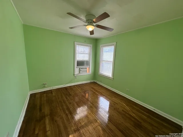 an empty room with wooden floor fan and a window