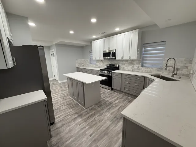 a large kitchen with stainless steel appliances a sink a stove a refrigerator a center island and furniture