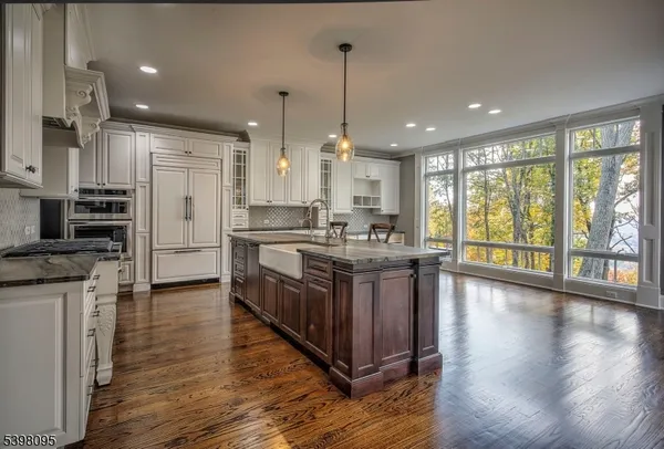 a kitchen with stainless steel appliances granite countertop a stove a sink a refrigerator and white cabinets with wooden floor