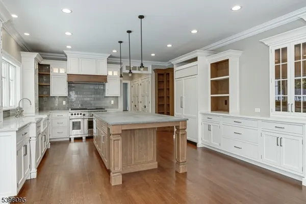a large kitchen with stainless steel appliances kitchen island granite countertop a large stove a sink dishwasher and white cabinets with wooden floor